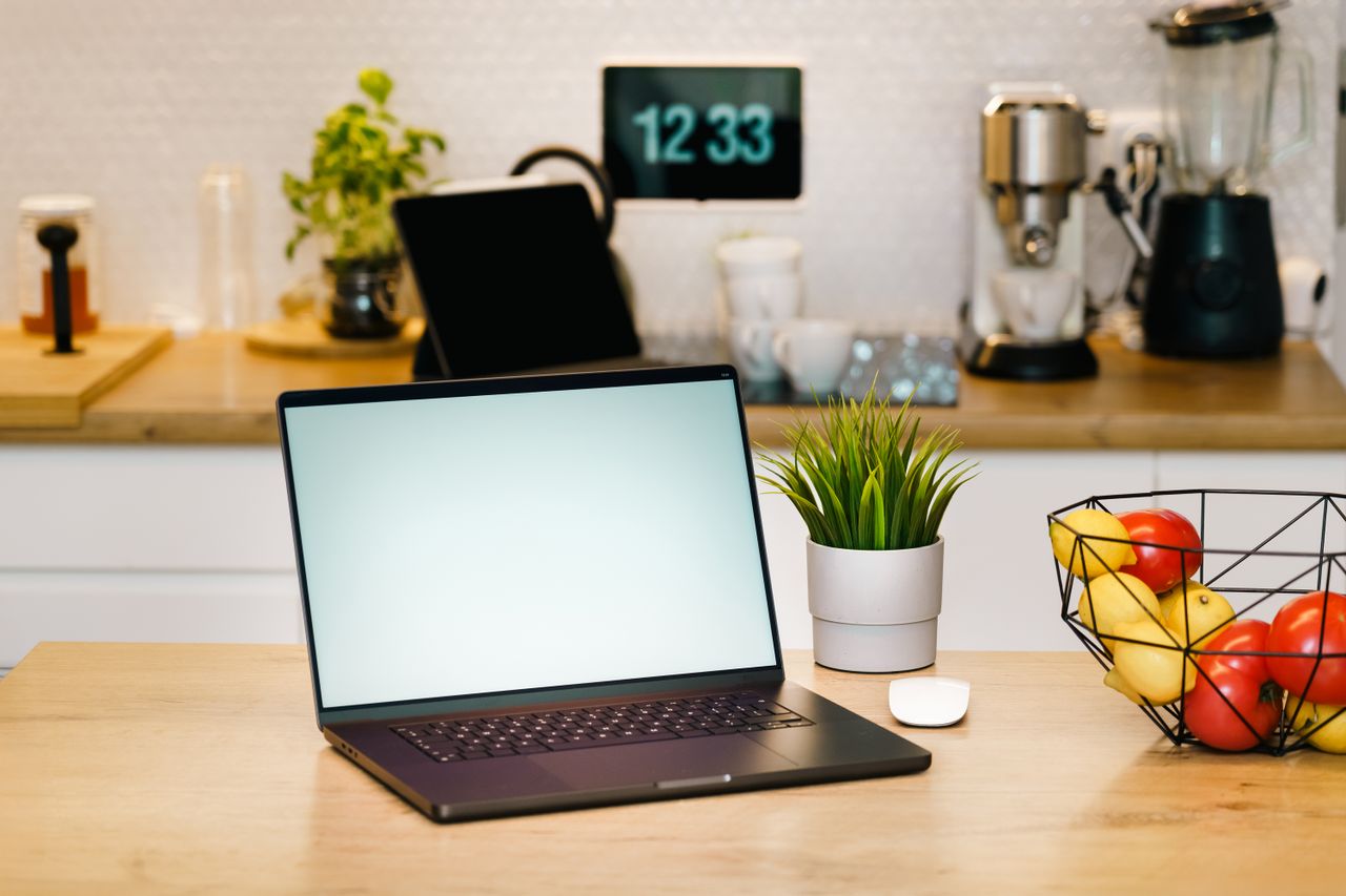 Home A modern kitchen workspace featuring a laptop, coffee machine, and fruit basket, ideal for remote work.
